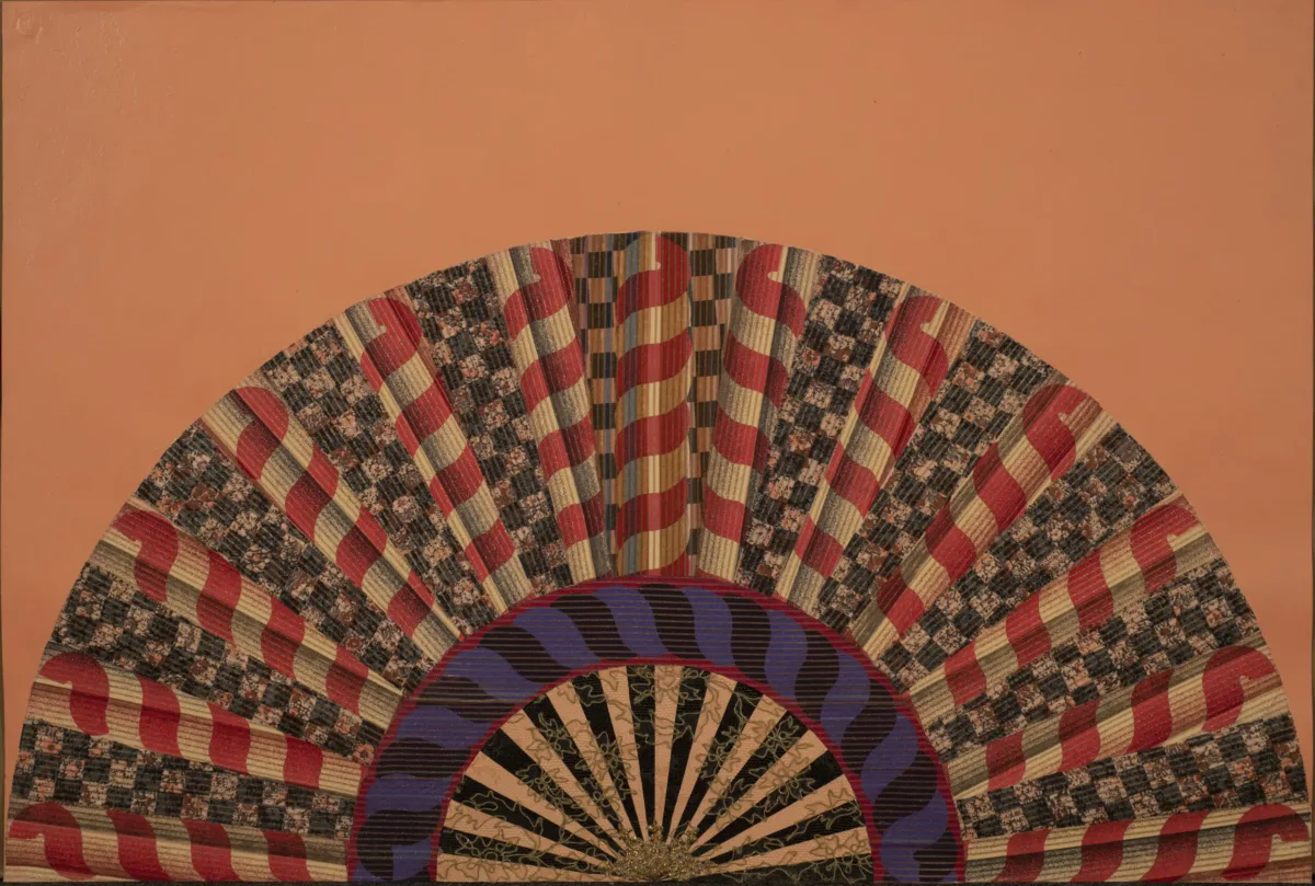 A colorfully painted and collaged folding fan spread open on a peach-orange background.