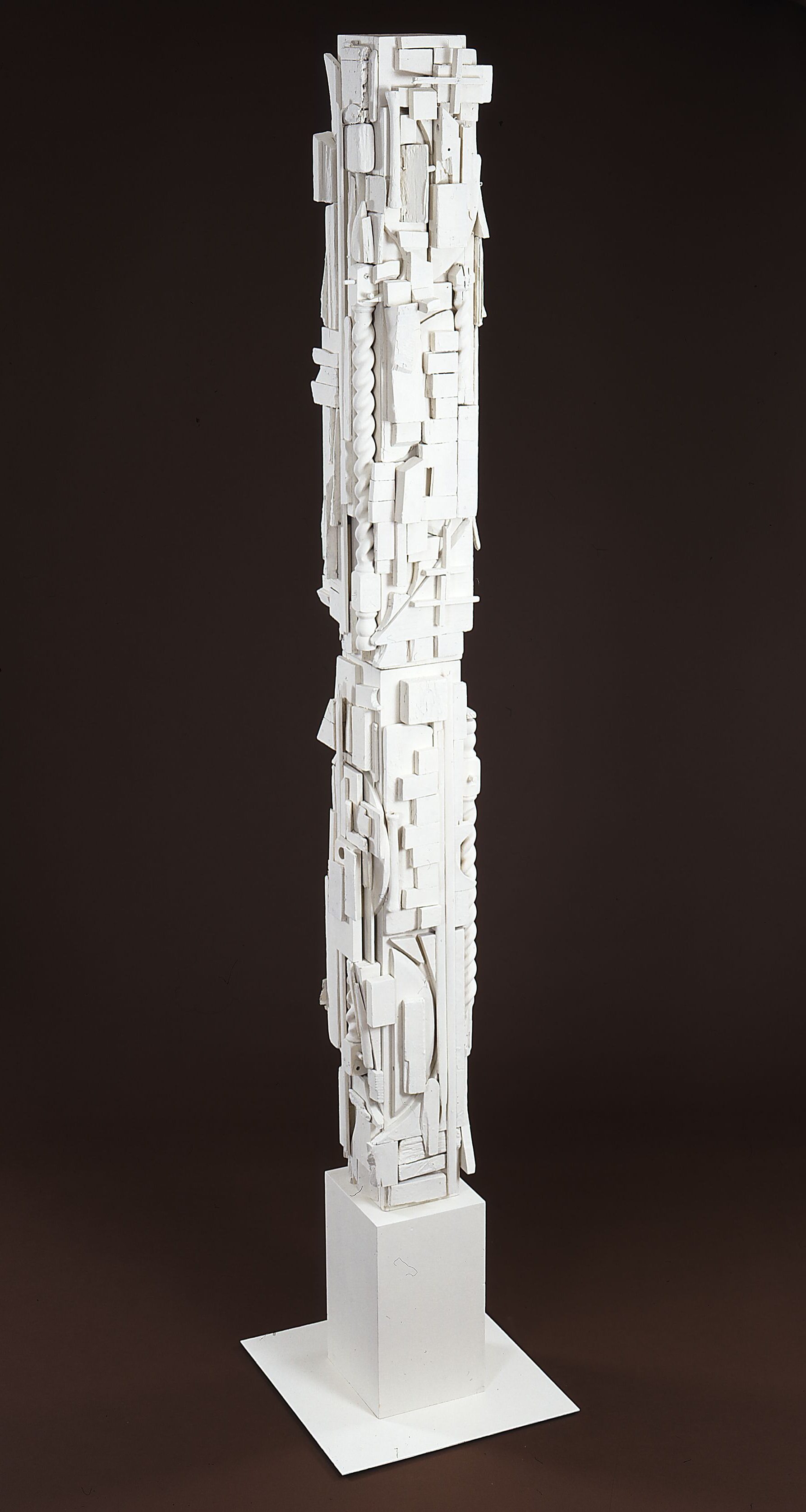 A tall, slender, rectangular column painted white and covered in geometric shapes of various sizes that come together to resemble decorative building components.