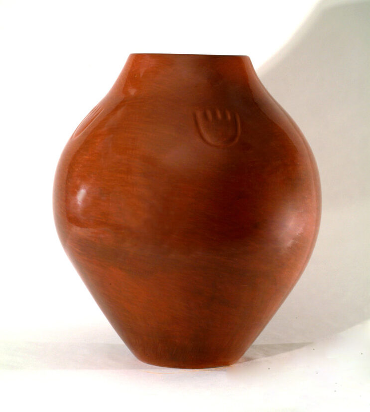 Red clay jar with a round shape that widens at its center. Its polished, warm-colored surface is decorated with a small paw print just below its top.