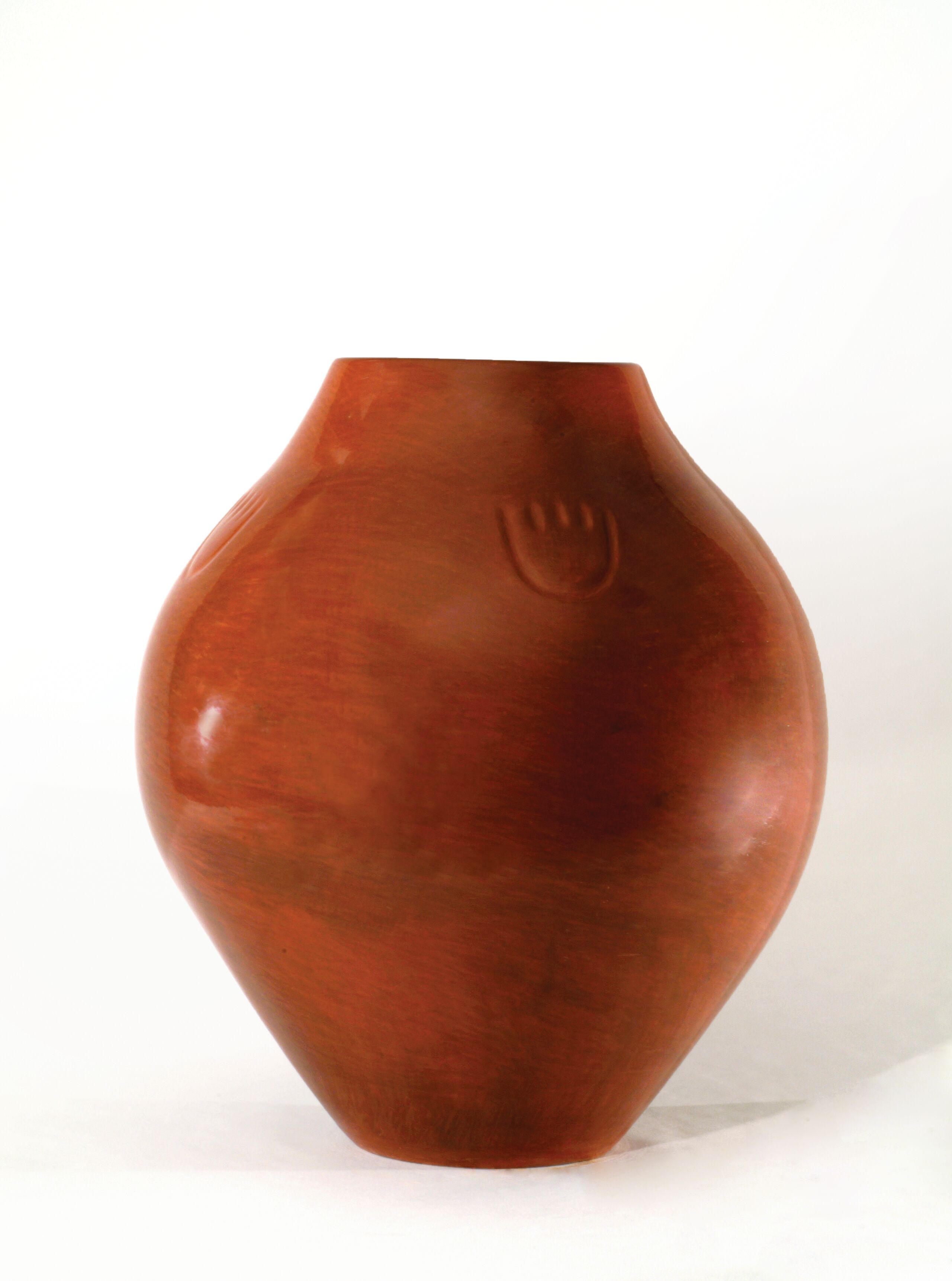 Red clay jar with a round shape that widens at its center. Its polished, warm-colored surface is decorated with a small paw print just below its top.