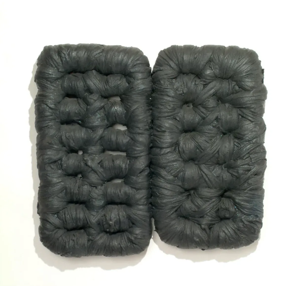 Wall sculpture featuring two rounded rectangular forms, the right slightly smaller than the left, resembling tufted cushions. The forms perimeters and interior sections are wrapped in fabric heavily coated with matte black latex paint, accentuating the tufts and folds of the fabric.