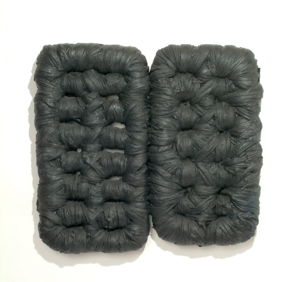 Wall sculpture featuring two rounded rectangular forms, the right slightly smaller than the left, resembling tufted cushions. The forms perimeters and interior sections are wrapped in fabric heavily coated with matte black latex paint, accentuating the tufts and folds of the fabric.