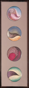 Four painted plates are displayed vertically against a mauve background within a brown frame. Each plate is painted with colorful swirls of pink, blue, brown, sand, and green. The painted shapes suggest abstract landscapes or organic forms.