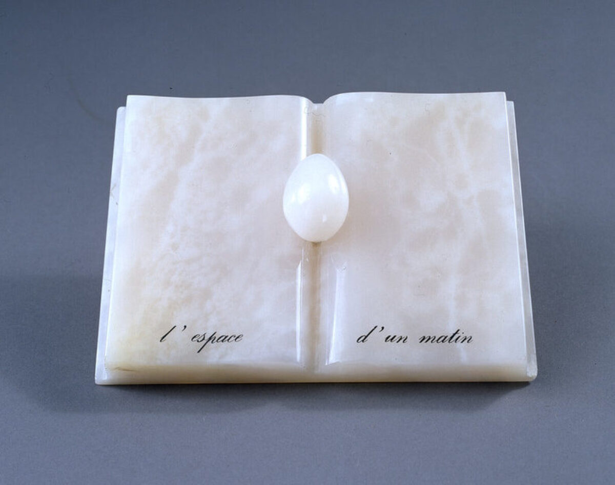 An open book with an egg nestled in the spine, all made of rose-colored onyx. An inscription in French painted in black at the bottom reads, "L’espace d’un matin" (The span of a morning).