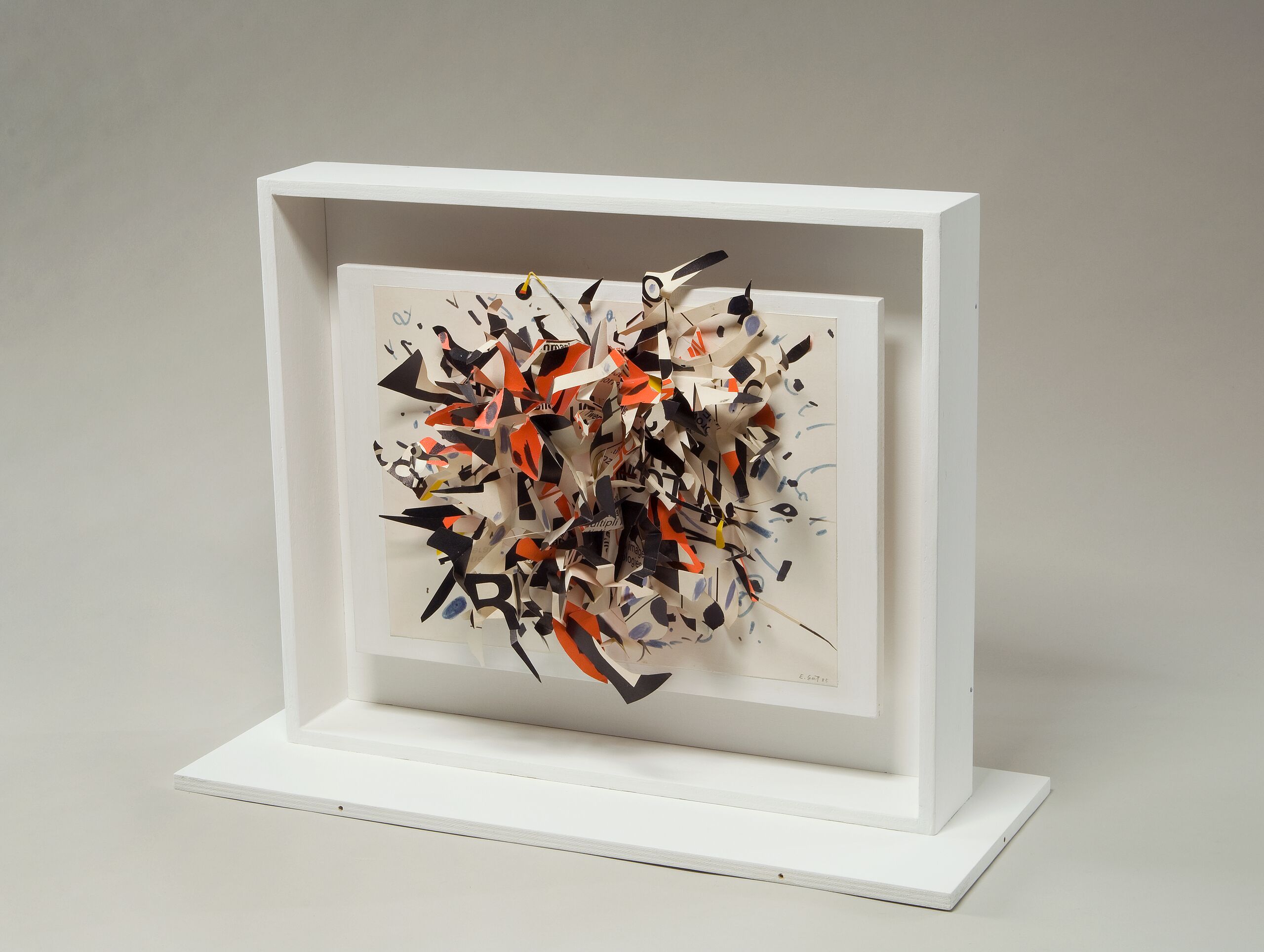 A three-dimensional collage explodes into space with cut-out shapes of black, red, white, and blue. Concentrated in the center, the piece dissipates towards the edges, with a bird's head peeking out of the morass towards the top. The canvas floats within a larger, white frame.