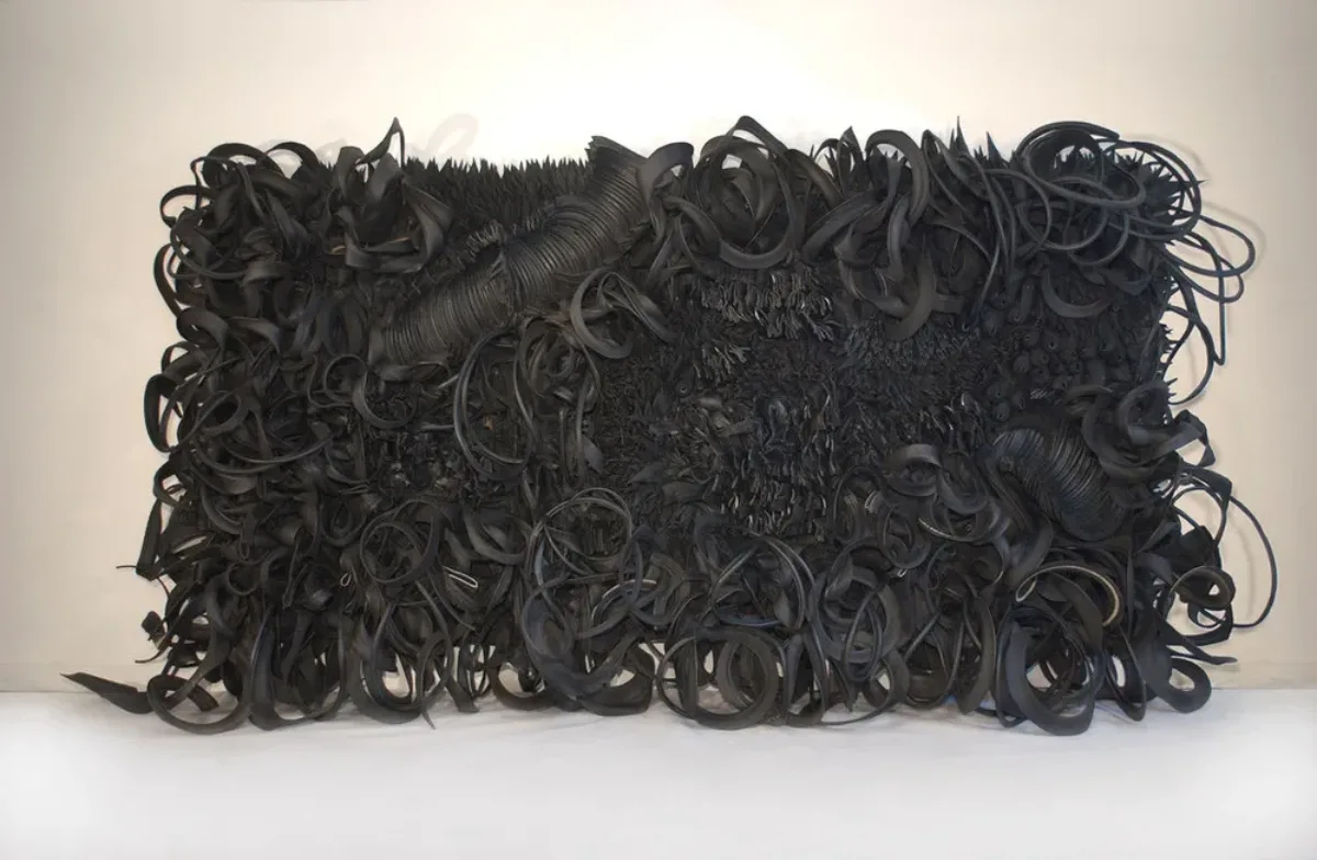 The wall-sized, horizontal sculpture consists of black rubber tires and tubing that has been sliced, stripped, woven, looped, twisted and otherwise manipulated into an expressive and abstract high-relief tableau.