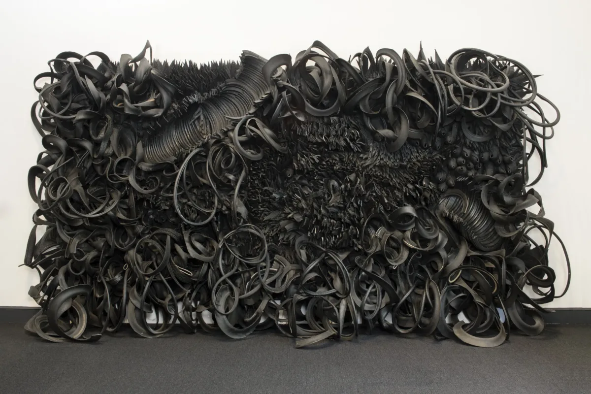 The wall-sized, horizontal sculpture consists of black rubber tires and tubing that has been sliced, stripped, woven, looped, twisted and otherwise manipulated into an expressive and abstract high-relief tableau.