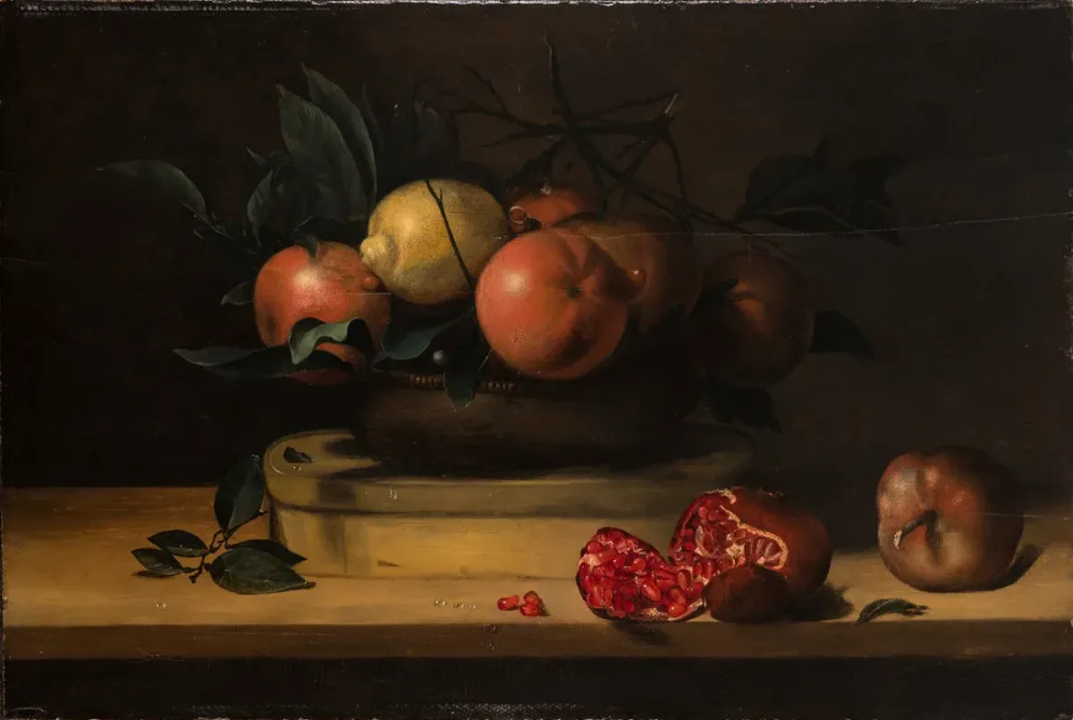 A vessel mounded with 5 oranges, a lemon, and greenery sits atop an oval, wooden box resting on a wooden plank. In the foreground, two pomegranates, one of which has split open and dropped three seeds, balance near the plank’s edge. Droplets of water dot the fruit and the table.