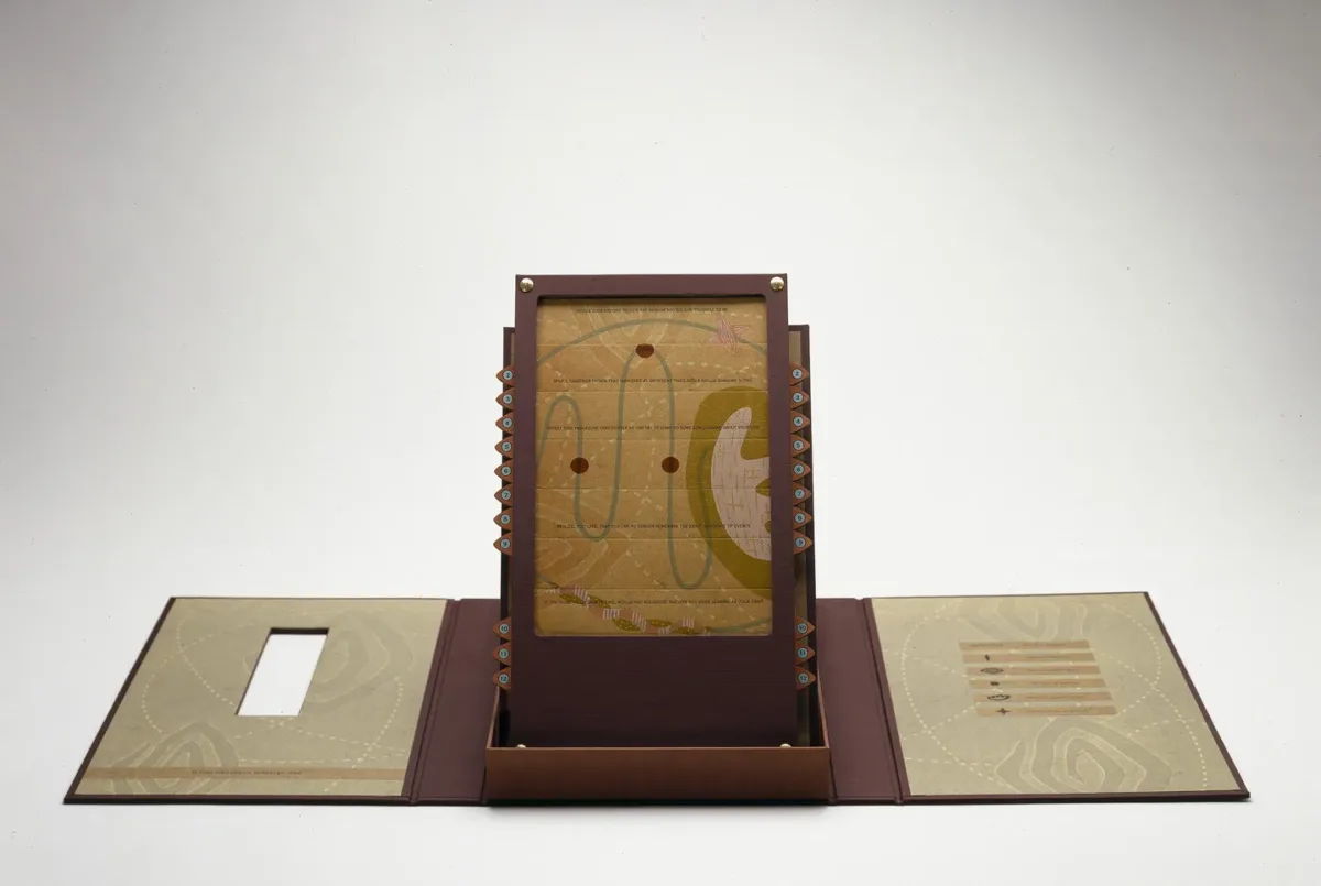 An open maroon portfolio with contents displayed upright in center. Upright panel is an abstract image with red circles connected by a curving green line on a mustard yellow background.