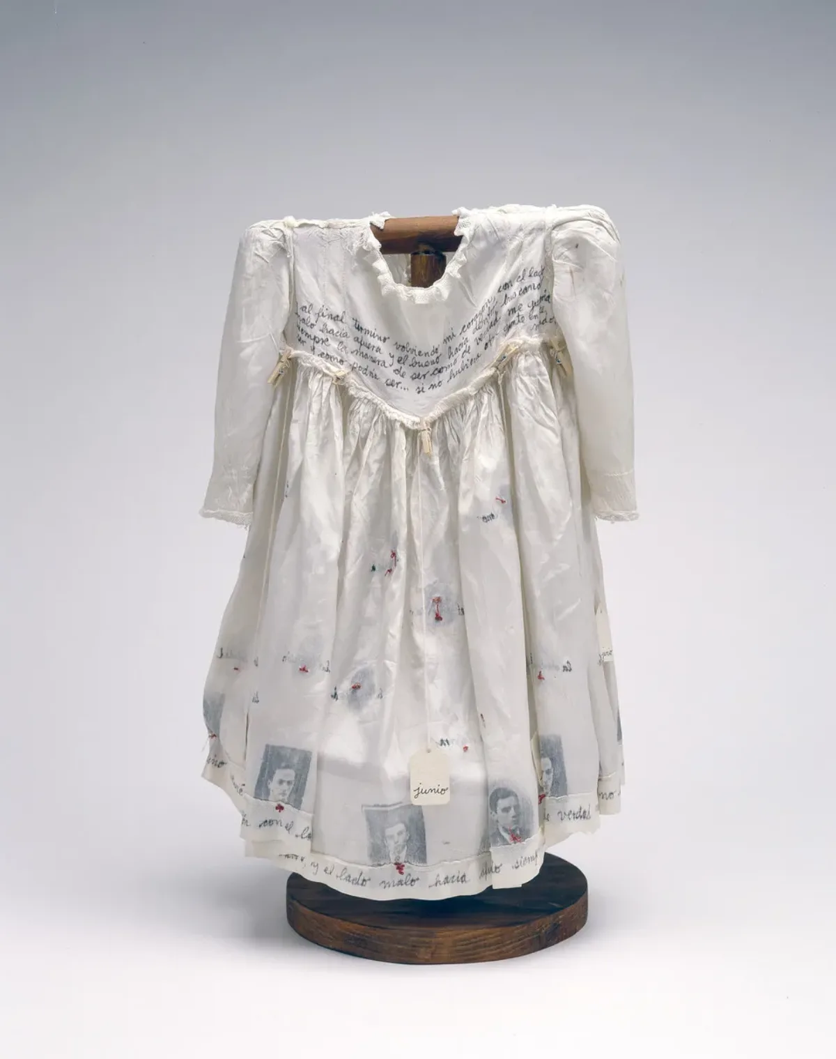 Hung on a dark wood, T-shaped form, a child's ivory-colored silk dress serves as a canvas for photographs, calligraphy, stitching, and the words of Anne Frank.