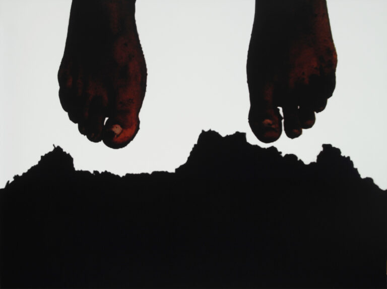 Two dark-skin-toned feet hang down from the top of the frame. The feet are covered in soil and mounded up just below them soil breaks up from the bottom of the frame.