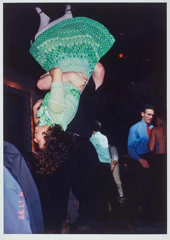 Color photograph of a woman in a green dress being flipped upside down by her dance partner dressed in black. Other couples are dancing in the background.