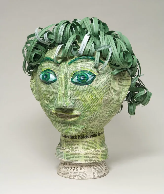 Papier-mâché head covered in clippings of pages from James Joyce's novel Ulysses. In varying shades of green, the head includes curly, lettered strips for hair and wide and classic-Greek-style eyes under arched eyebrows.