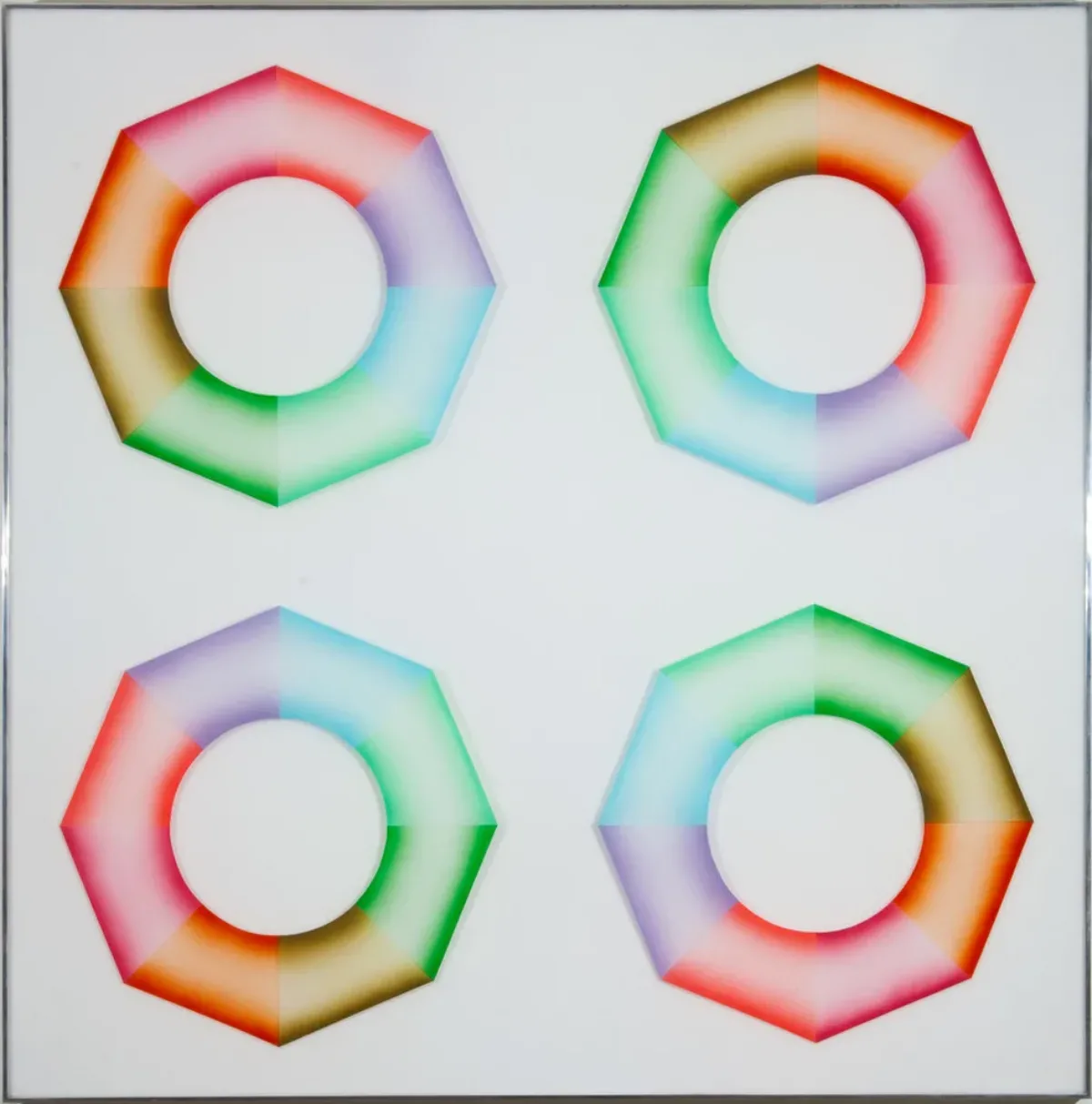 Four hard-edged octagonal rings, divided into wedges of brown, orange, pink, red, purple, blue, mint green, and grass green, sit on a square, white surface. Dark at the inner and outer edges and light in the center, the colors create the illusion of curved 3-dimensional objects.