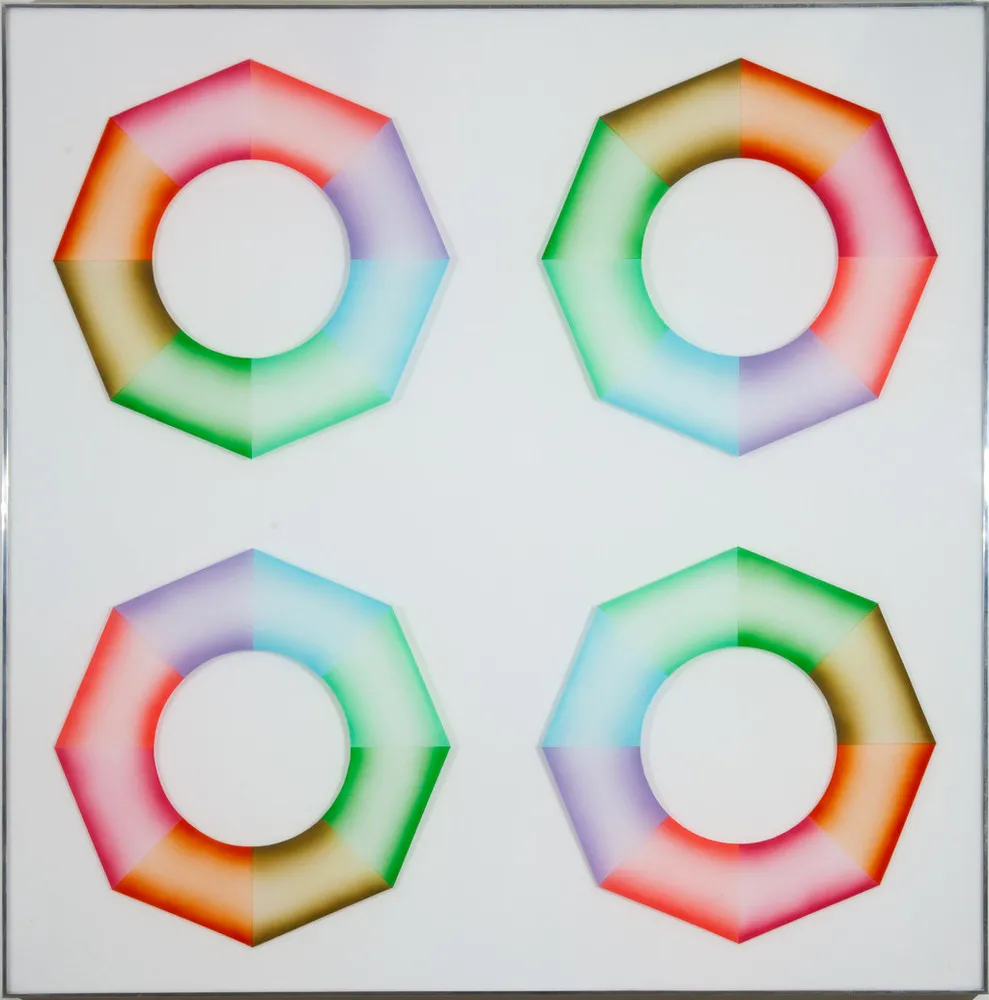 Four hard-edged octagonal rings, divided into wedges of brown, orange, pink, red, purple, blue, mint green, and grass green, sit on a square, white surface. Dark at the inner and outer edges and light in the center, the colors create the illusion of curved 3-dimensional objects.