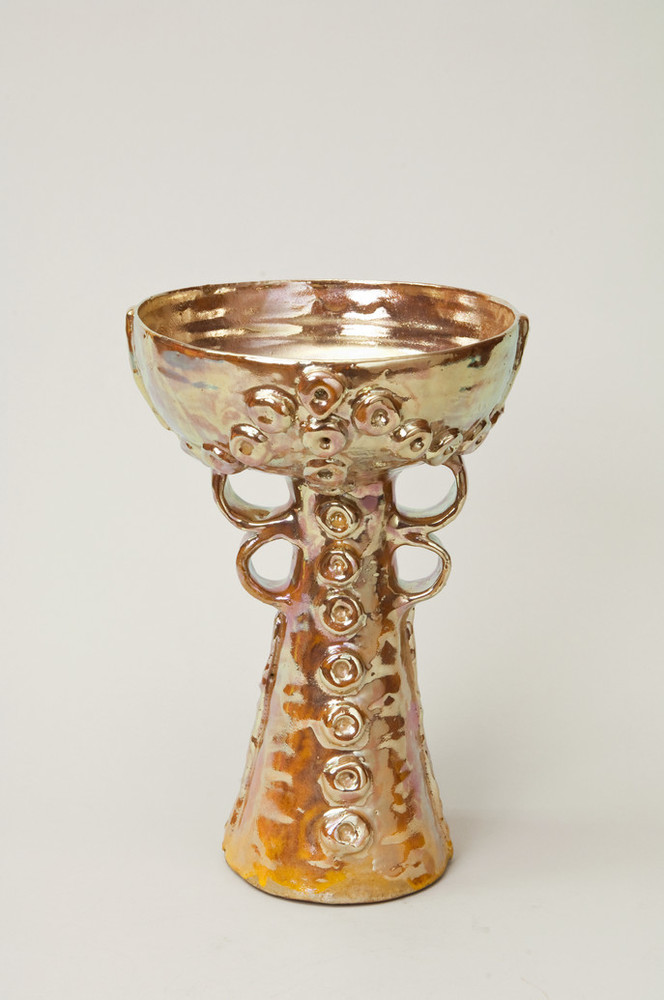 Golden lusterware chalice features a wide bowl above two looped handles on either side of the cone-shaped base. Raised circular decorations adorn the base and the outside of the bowl.