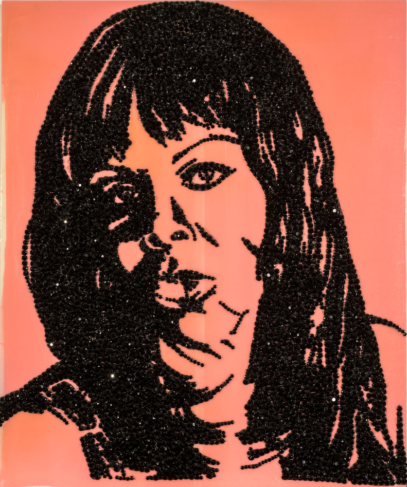 A mixed-media artwork renders the contours of an African American woman’s facial features, shoulders, and long, straight hair in black rhinestones on a glossy, bubble-gum pink panel. The woman faces forward, gazing outward. Some rhinestone facets glint with reflected light.