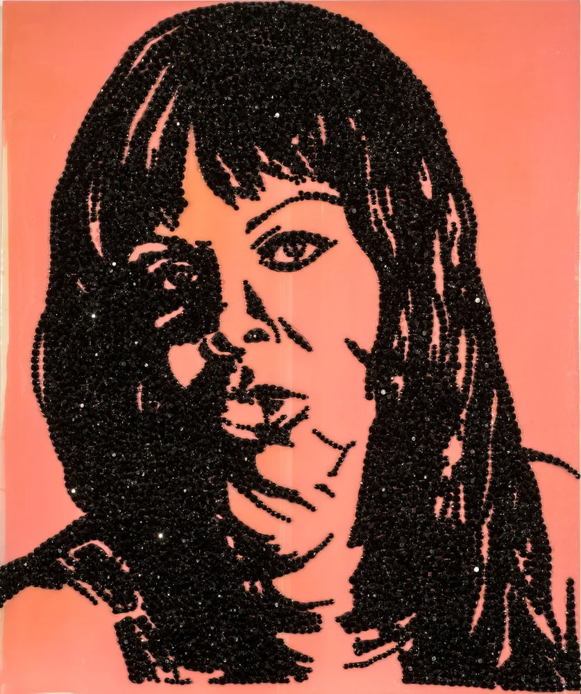 A mixed-media artwork renders the contours of an African American woman’s facial features, shoulders, and long, straight hair in black rhinestones on a glossy, bubble-gum pink panel. The woman faces forward, gazing outward. Some rhinestone facets glint with reflected light.