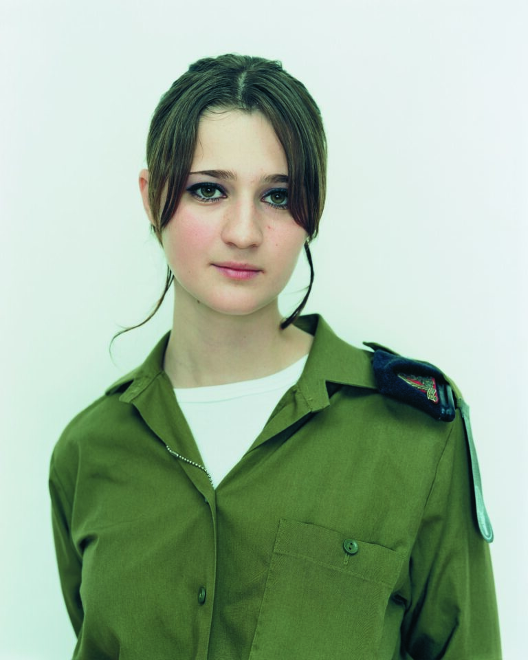 Paired photographic portraits capture a young, light-skinned woman at different life moments. At left, she wears a black sweater and gazes out shyly from beneath her dark bangs. At right, clad in an olive drab, military shirt, she makes eye contact with viewers more confidently.