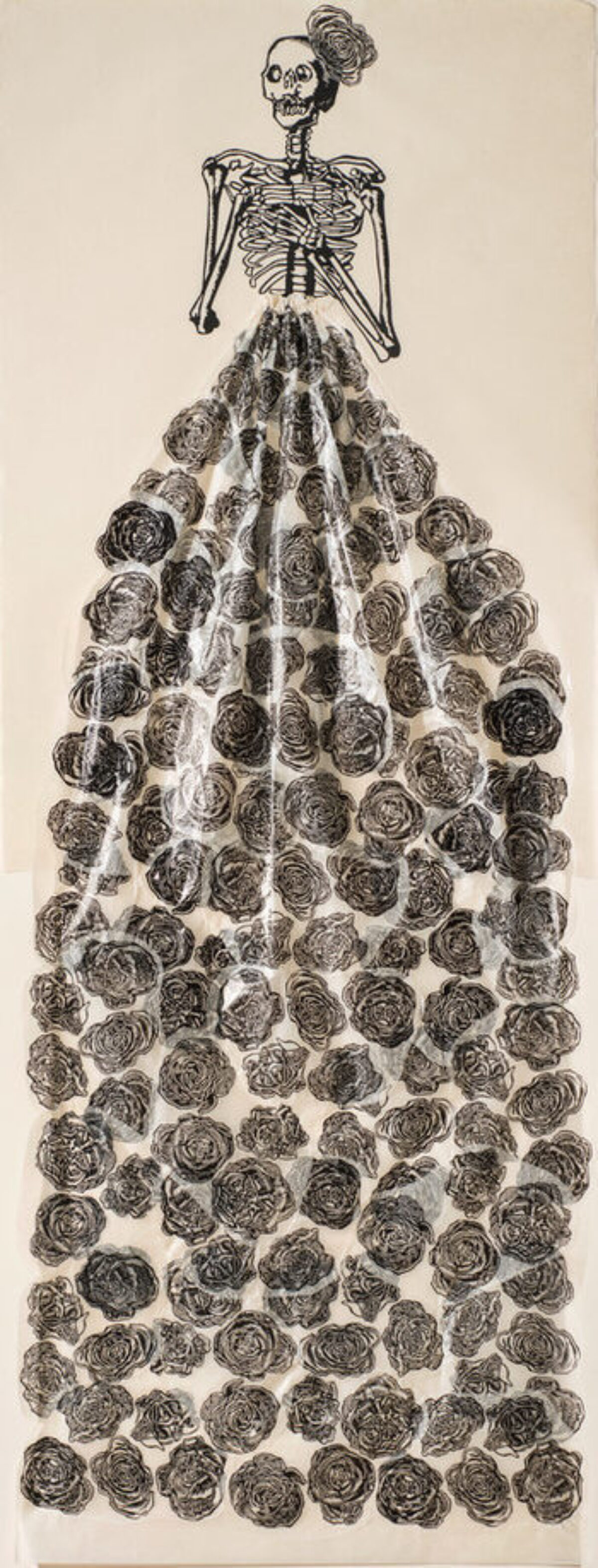 A very tall and narrow, black-and-white print pictures a skeleton with folded arms, a rose fascinator perched on its head. The figure wears a collaged, three-dimensional, billowing skirt made of tissue and printed with roses.