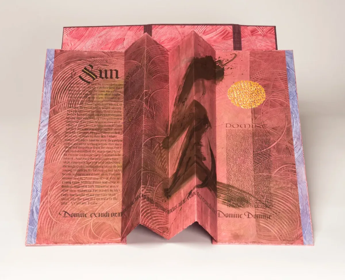 An open, accordion-style book with red-pink pages and black text. The word "Sun" is written in large, Gothic print at the upper left. At center-right is a large, black brushstroke that extends the length of the page. At the upper right is a golden circle.