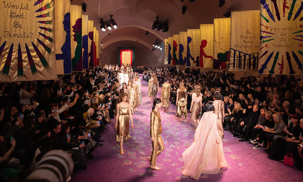 Models walk the final act of Dior's couture show against Judy Chicago's backdrop of embroidered feminist banners.