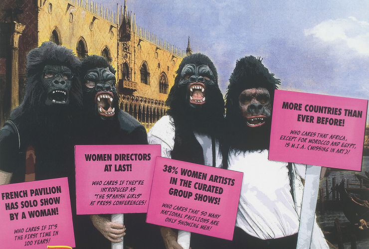 Four figures stand side by side and wear gorilla masks that cover their entire heads. The background shows a sunlit building with arched windows, sky, and in the lower right corner a small glimpse of water and the tip of a gondola. Each guerilla holds a pink sign with black text.