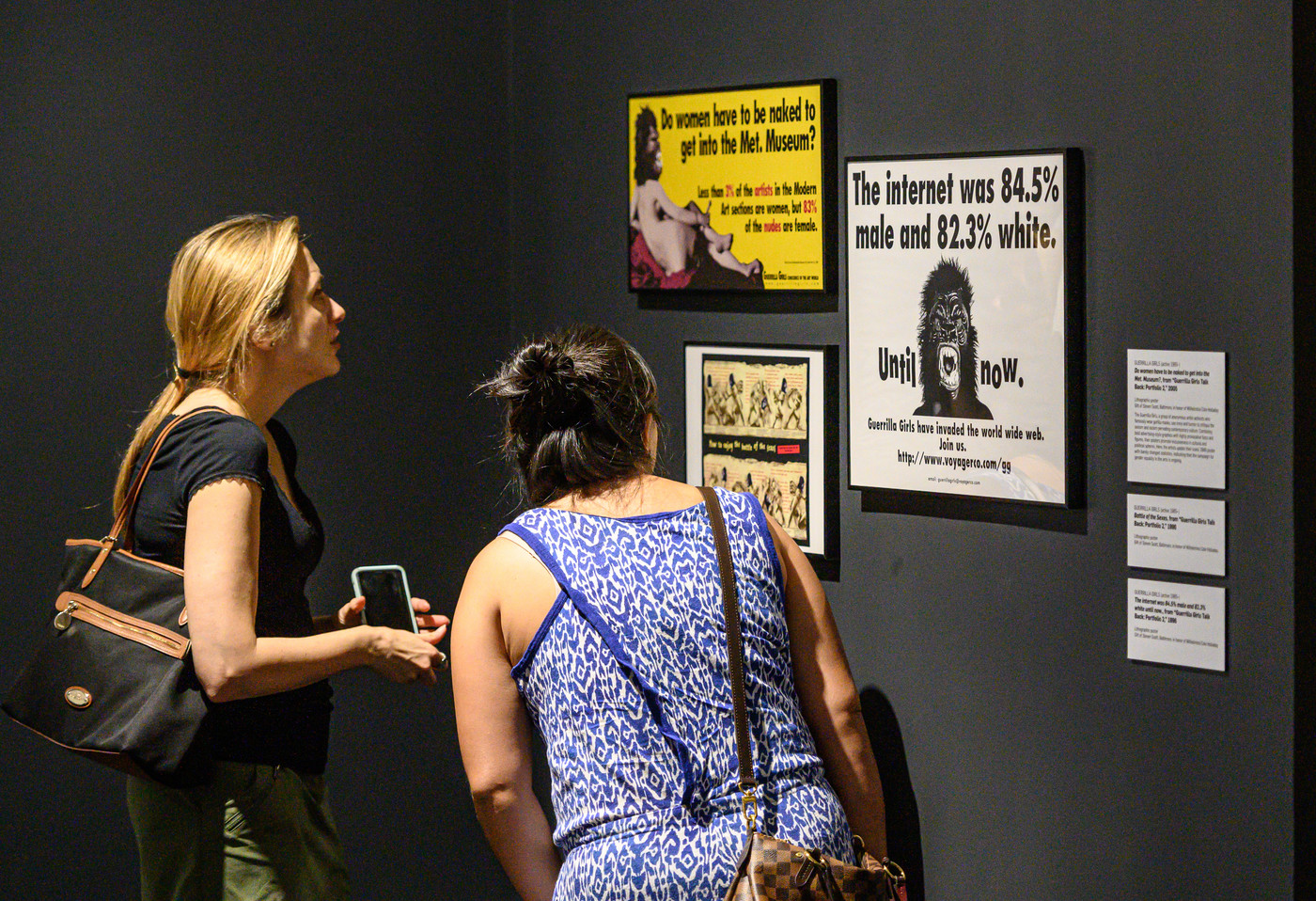 Two women look closely at artwork on the gallery wall.