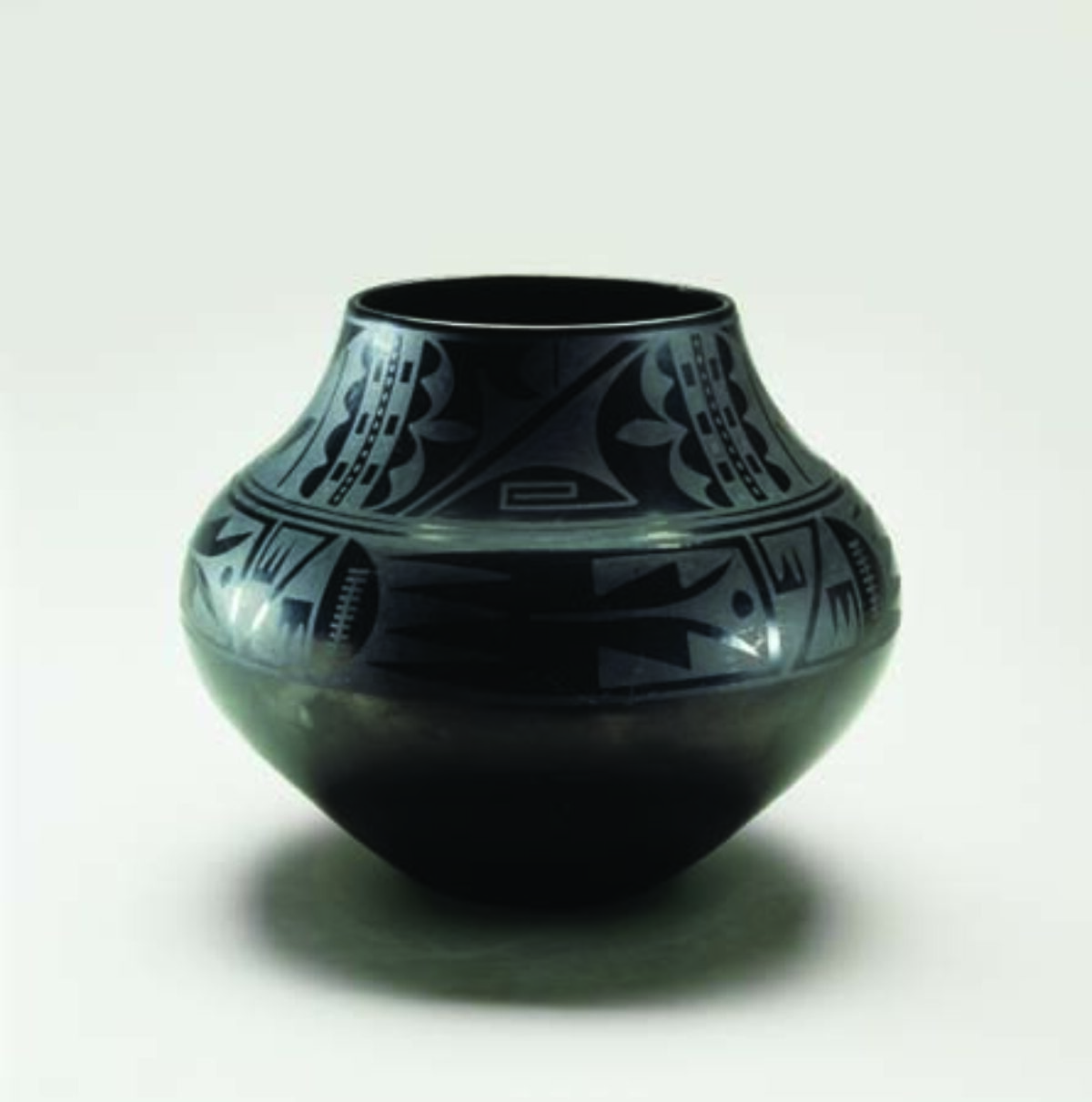 Blackware pottery vessel with a wide mouth and bulbous body that tapers to a narrow base. The pot is adorned with geometric tribal patterns presented in a matte finish on the glossy surface.
