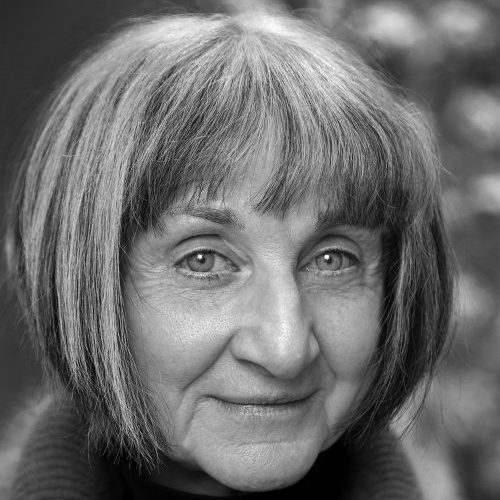 A black-and-white photograph of a light-skinned adult older woman seen from the chin up. She has a salt-and-pepper bob haircut and wears a dark turtleneck.