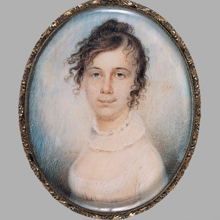 An oval painting in a delicately detailed frame with a protective resin cast over it depicting a light-skinned adult woman smiling gently. She wears a white dress and slightly frilled collar, and her curly dark hair is pulled up but also appears slightly windswept.