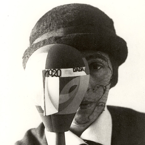 Black and white photo of a light-skinned woman in a black bowler hat, dark jacket and white collar. A layer of black lace and a round object with 1920 and Dada written on it obscure half of her face leaving only the left side visible.