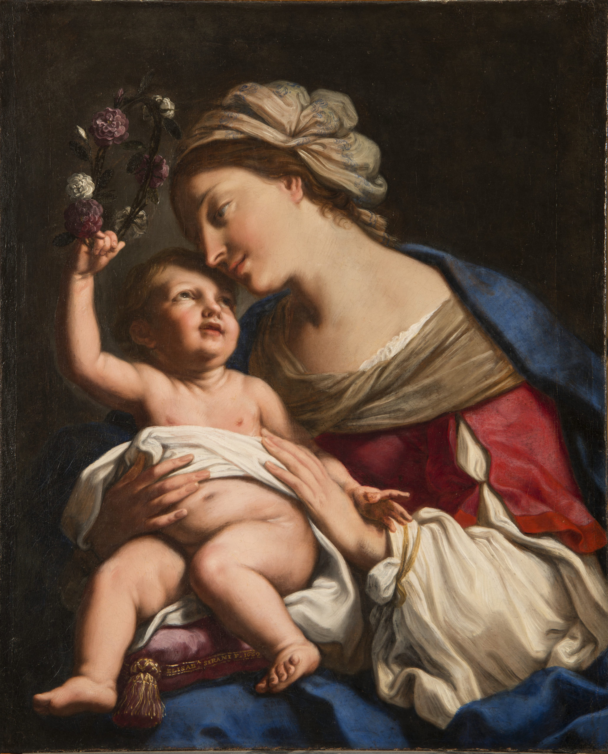 A young, light-skinned, brunette woman gazes down lovingly at the plump baby she holds on her lap. She wears a loose, tan turban, vivid blue cloak, and red dress with white sleeves. The light-skinned child returns her gaze, leaning back to crown the woman with a circlet of roses.