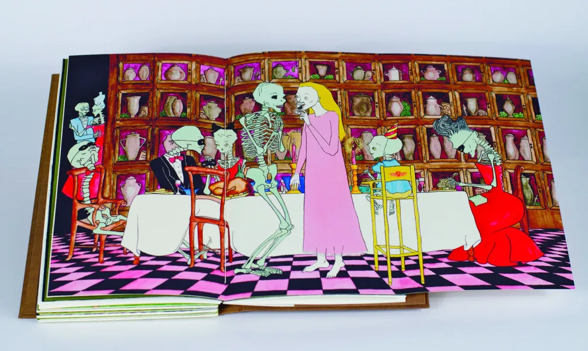 The open page of a book depicts a dinner party, attended by well-dressed skeletons, set in front of shelves of urns. In the foreground, a blonde woman wears a long, pink dress and sips red wine, engaging in conversation with a skeleton.