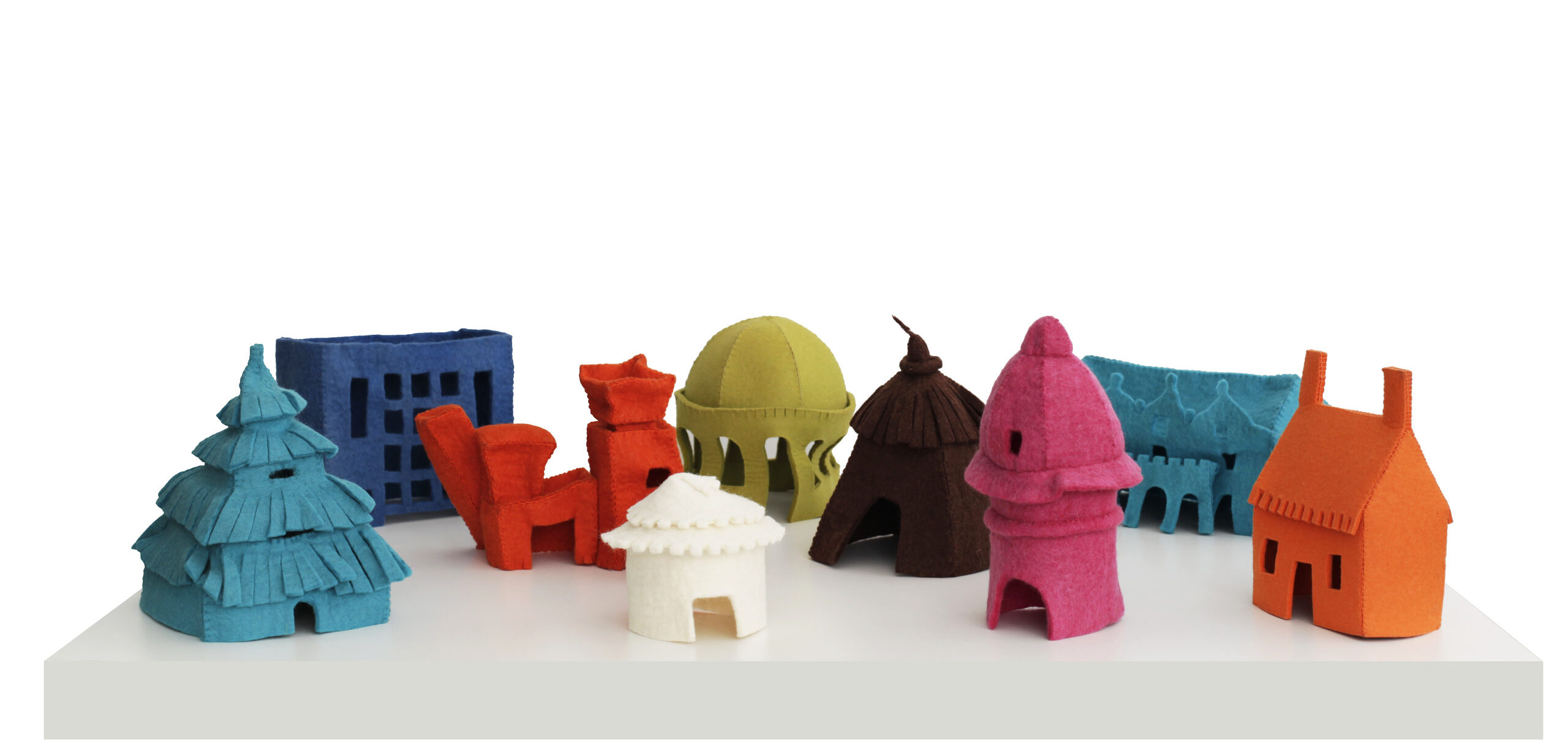 Arrangement of nine small, felt houses on a white table. Each house is a different, vibrant color and represents a different style of architecture spanning time and cultures—including a hut, a yurt, a cottage, art deco, postmodern architecture, and more.