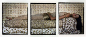 A woman lying on her back gazes confidently out at viewer adorned and surrounded by polished bullet casings