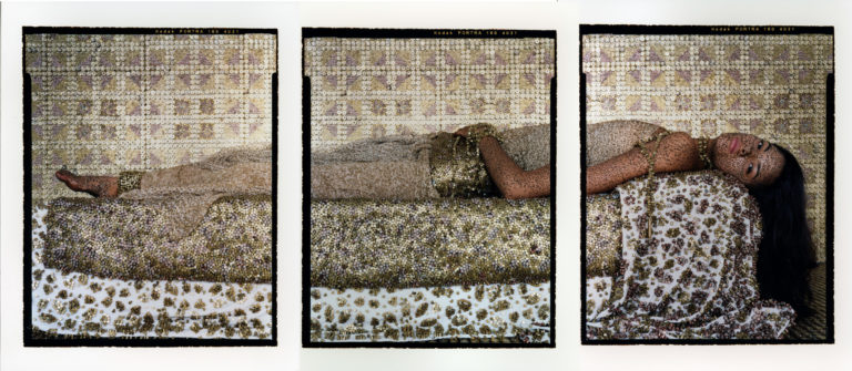 A woman lying on her back gazes confidently out at viewer adorned and surrounded by polished bullet casings