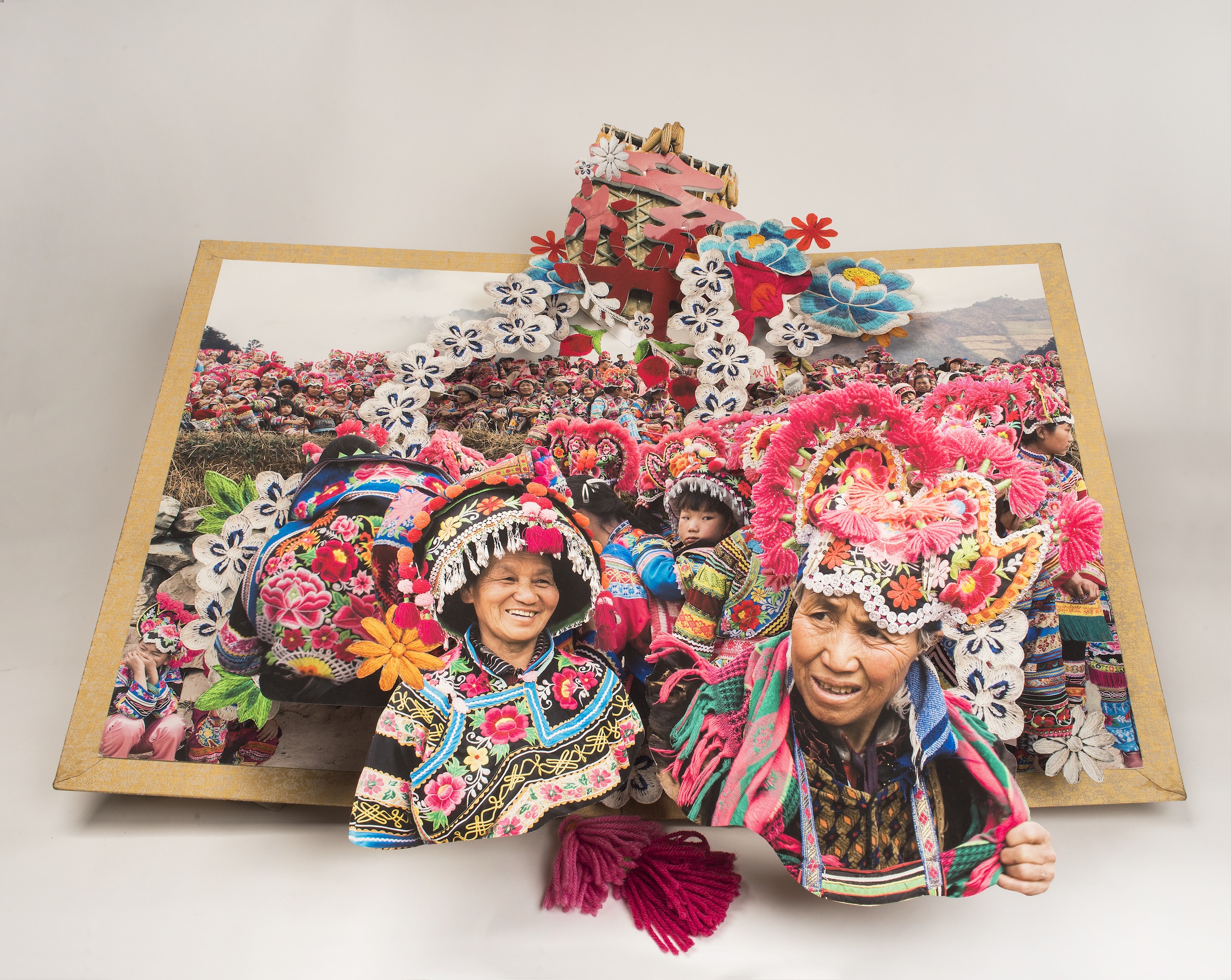 Large-scale pop-up book depicts the culture and traditions minority areas in China by showing numerous people in brightly colored, traditional dress.