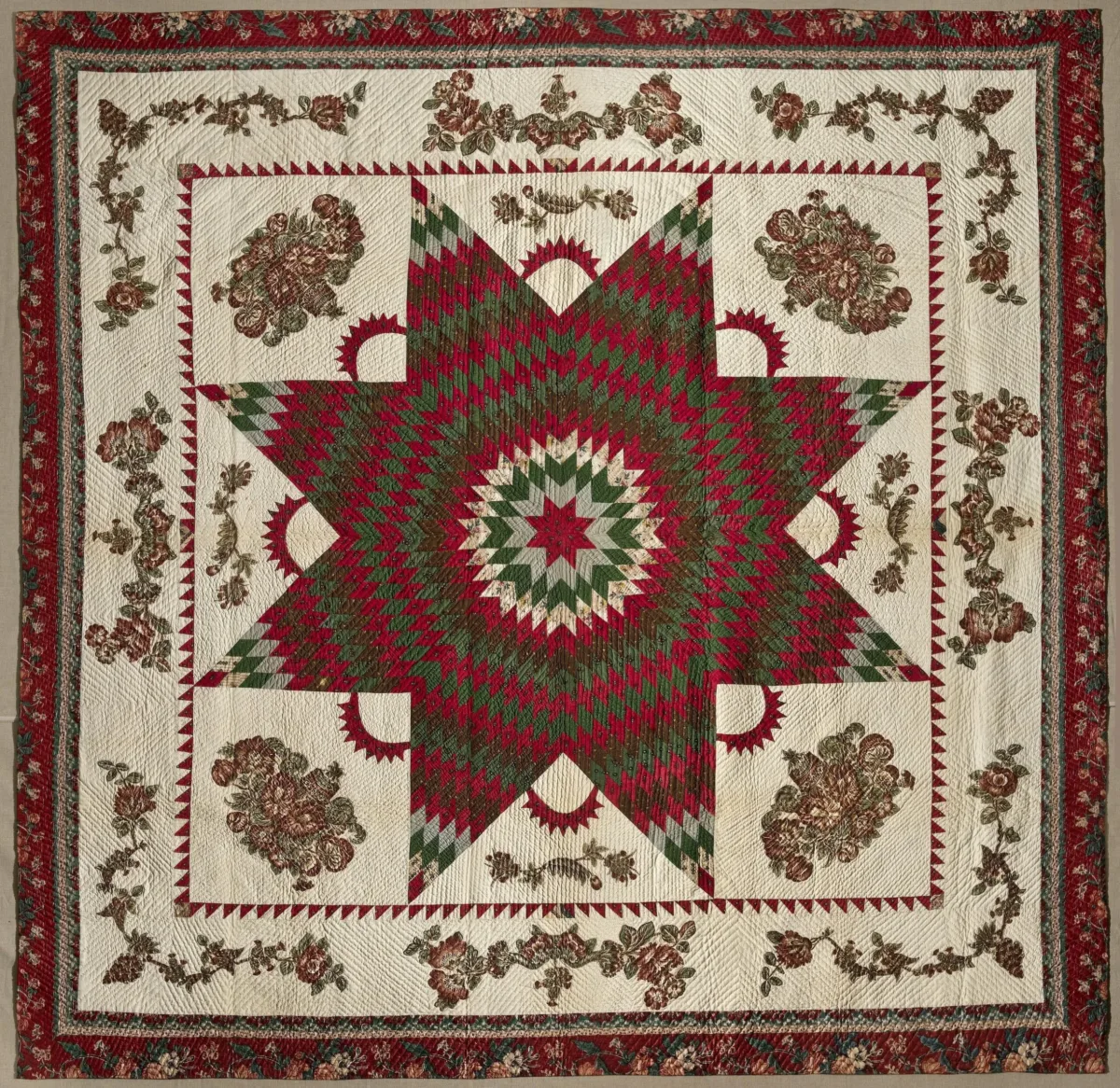 Vintage quilt in dark reds and greens on a cream background. In the center is a large eight-point Star of Bethlehem surrounded by Victorian floral appliques. The border, edged in dark red fabric, features matching floral garland appliques.