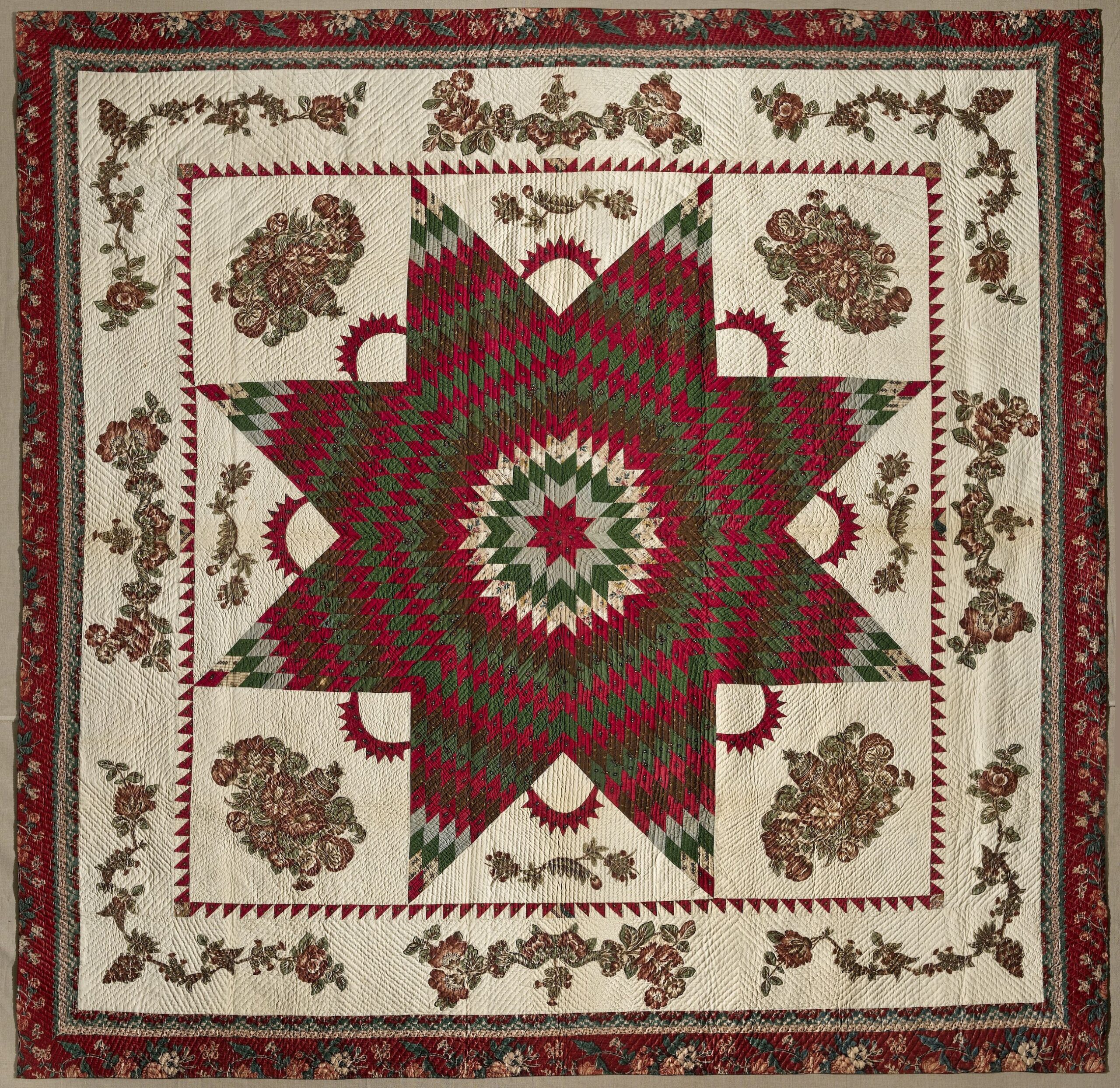 Vintage quilt in dark reds and greens on a cream background. In the center is a large eight-point Star of Bethlehem surrounded by Victorian floral appliques. The border, edged in dark red fabric, features matching floral garland appliques.