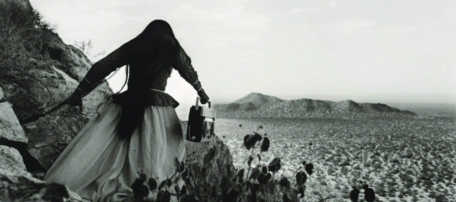 A black-and-white photograph of a woman dressed in white with white wings on her back walking.