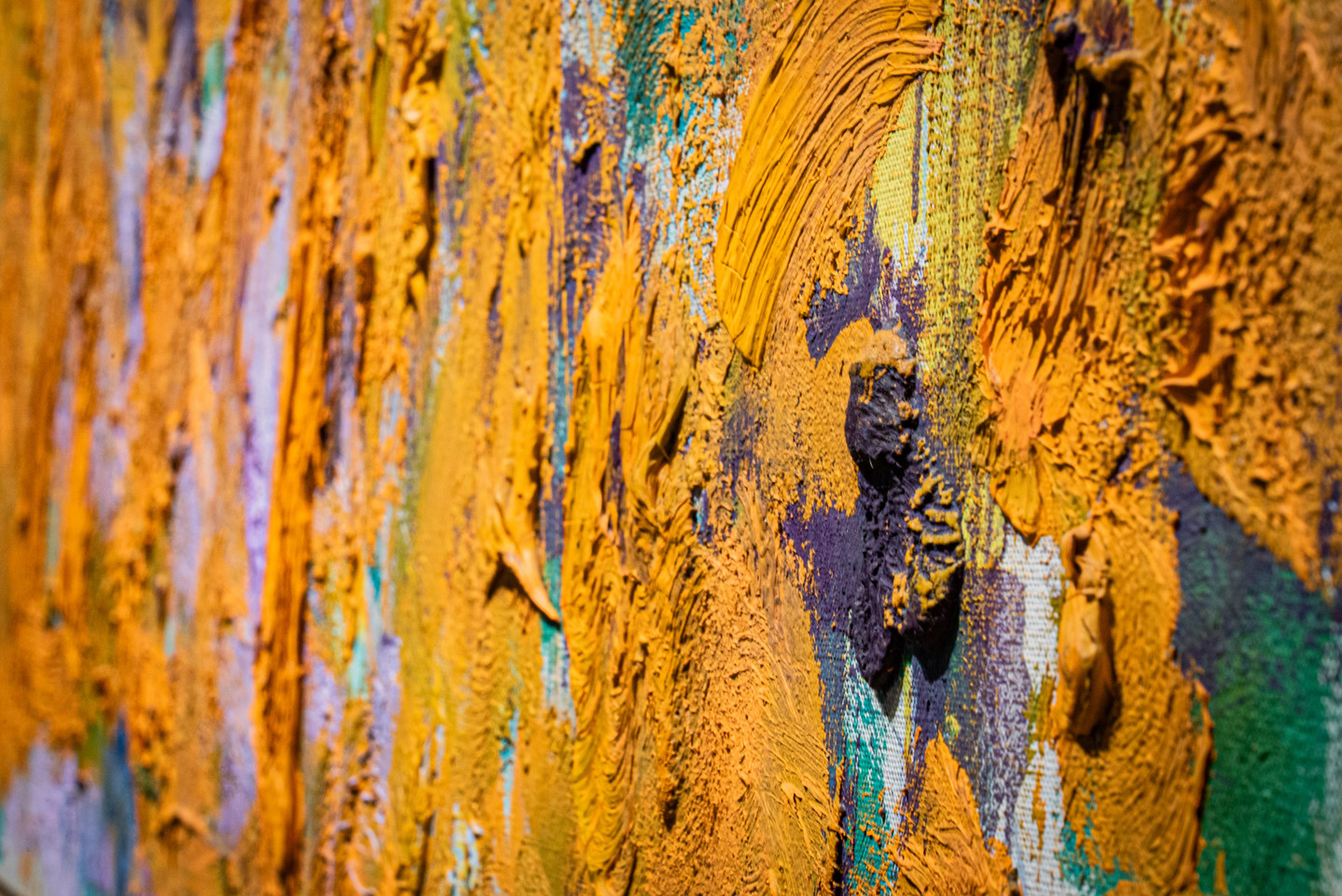 Close-up detail of an abstract painting with very thick and gestural brushstrokes of mostly orange paint.