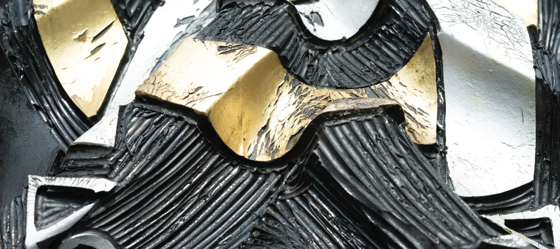 Closeup detail of an engraved tire with peeling ribbons of gold and silver leaf intertwined with varying directions of ribbed black lines.