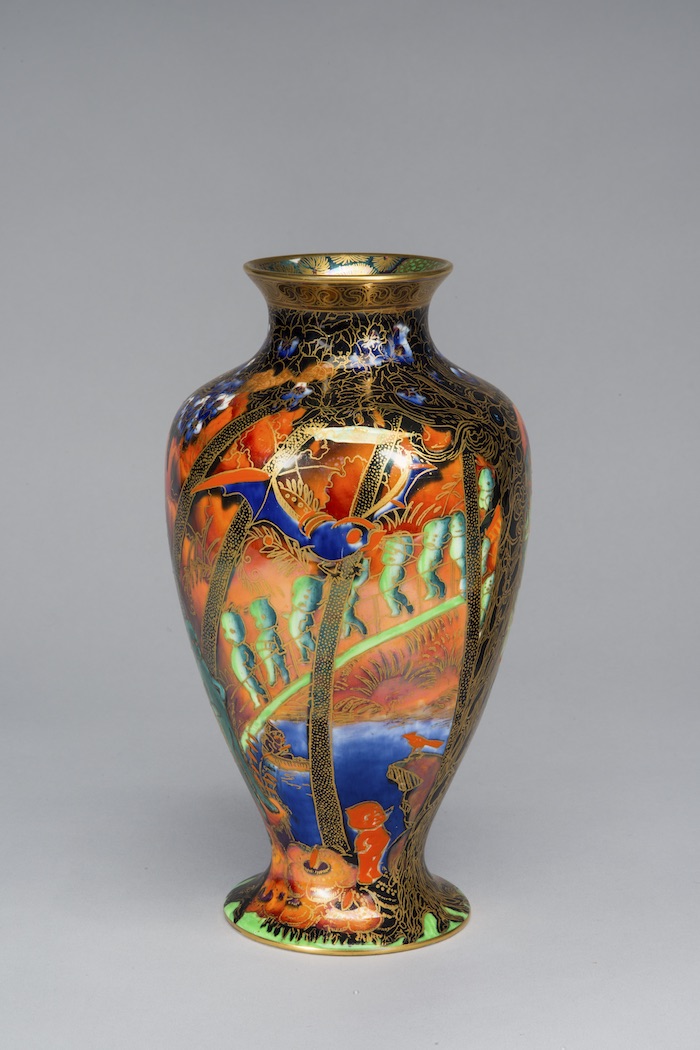 Iridescent lusterware vase features gold cloisonne and an ornamental Art Nouveau design. Against a vibrant orange background, the long twisted trunks of forest trees surround the vessel. A blue bat circles the treetops, while a procession of odd cherubic figures descends along a draping vine.