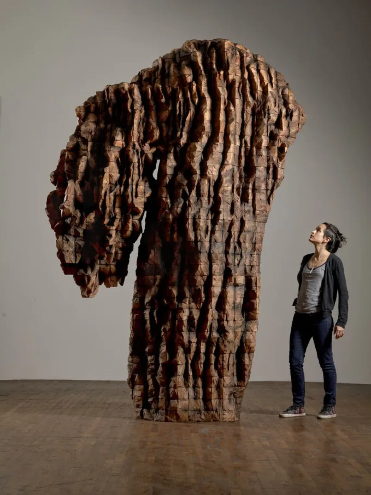 Female visitor with light skin looks up at a roughly 20 foot tall carved cedar sculpture.