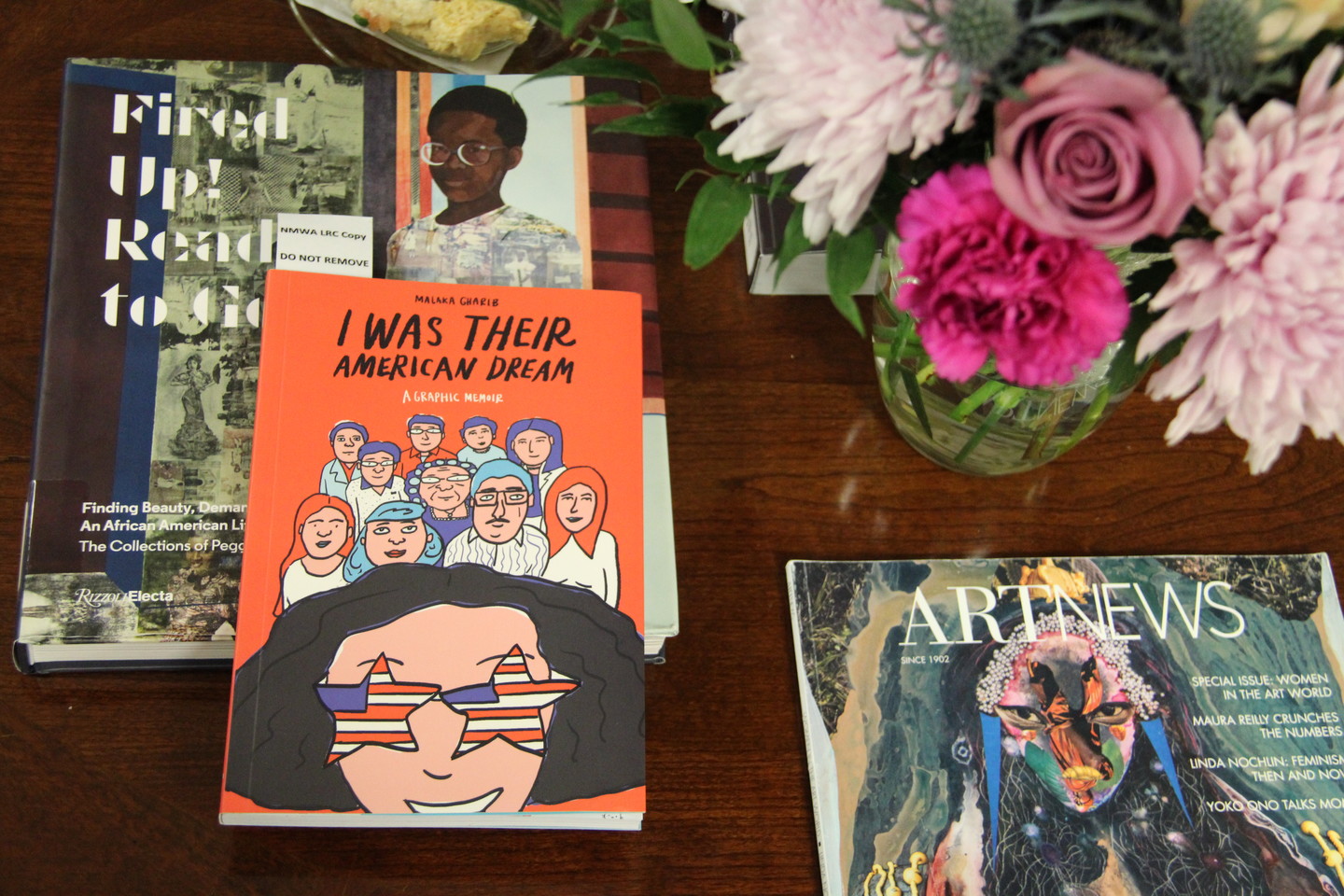 Two books, Fired Up! Ready to Go and I Was Their American Dream, rest on a tabletop, along with a small vase of pink and lavender flowers.