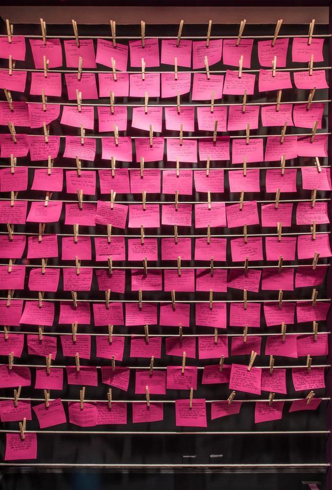 Wall of hot pink post-it notes hung on rows of string with clothespins.