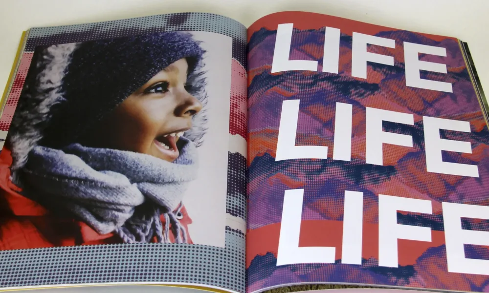 Open book features photograph of a child with medium-brown skin on the left side of the fold and the words "LIFE LIFE LIFE" filling the page on the right.