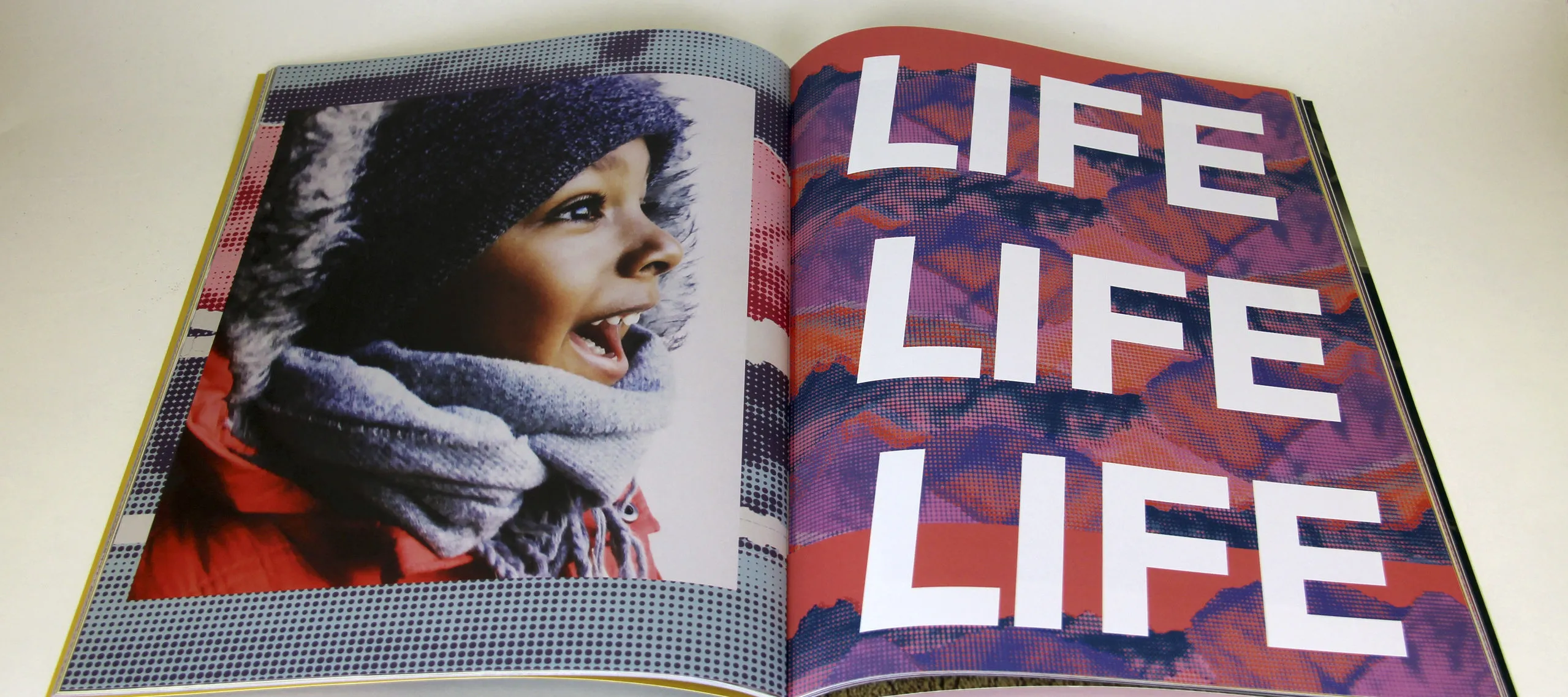 Open book features photograph of a child with medium-brown skin on the left side of the fold and the words "LIFE LIFE LIFE" filling the page on the right.