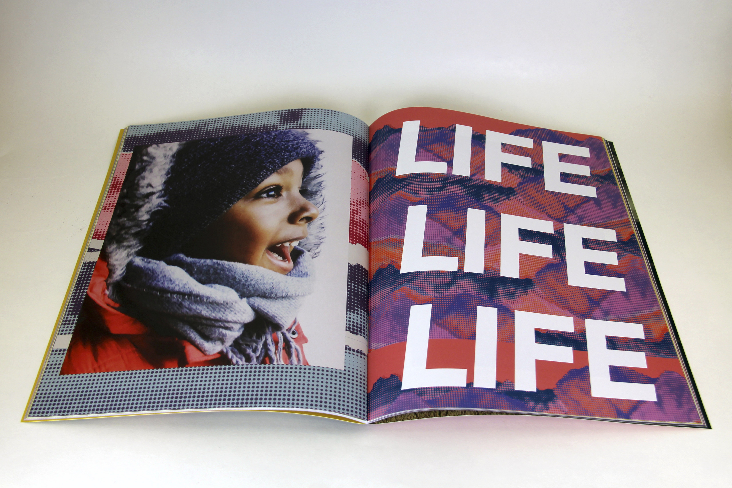 Open book features photograph of a child with medium-brown skin on the left side of the fold and the words "LIFE LIFE LIFE" filling the page on the right.